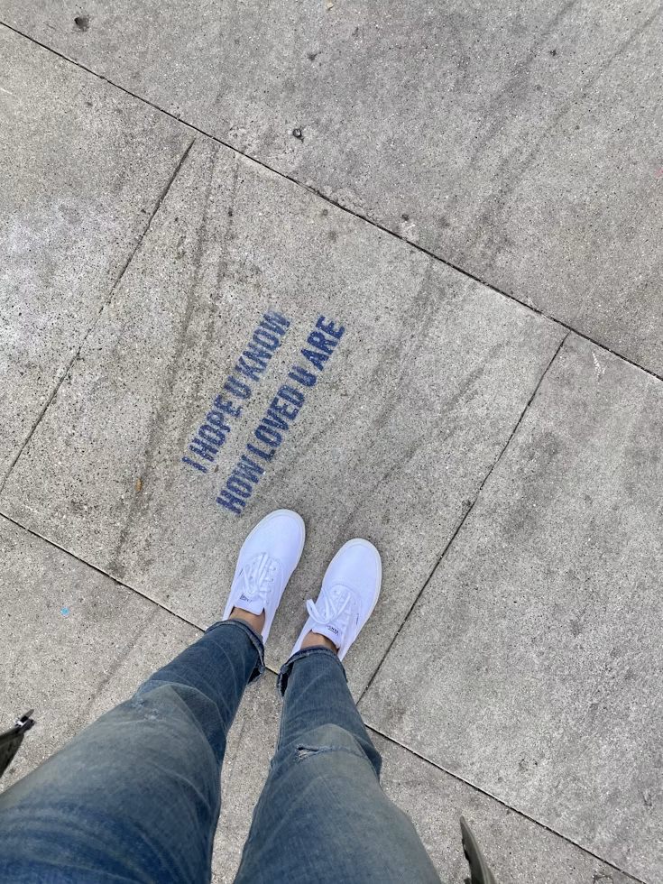 Words written on a footpath beside a pair of feet