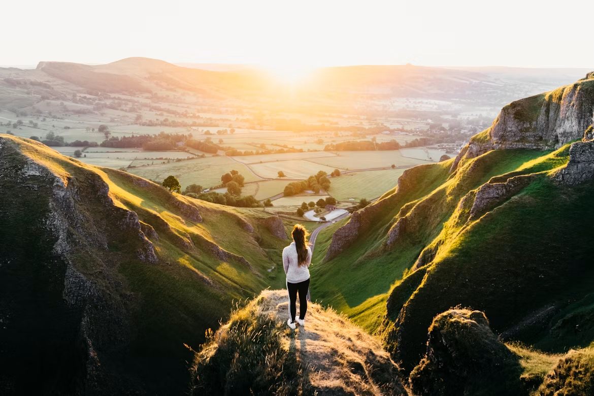 A person standing on a hilltop looking over a valley at sunrise