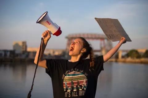 A young woman shouting into a megaphone and holding up a sign